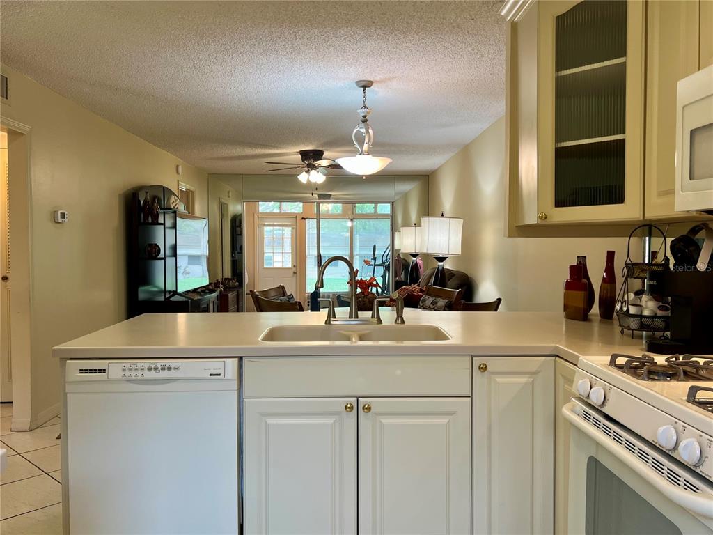 A kitchen island with a double sink overlooks a living area with a mirrored wall — 1395 MISSION DRIVE W UNIT 28C, CLEARWATER, FL