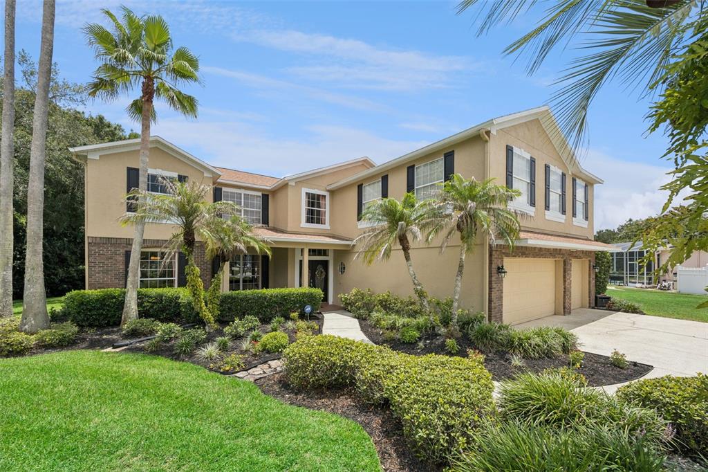 A two-story suburban house with a tan stucco exterior, brick accents, and a three-car garage — 1267 OAKFORD PLACE, OVIEDO, FL