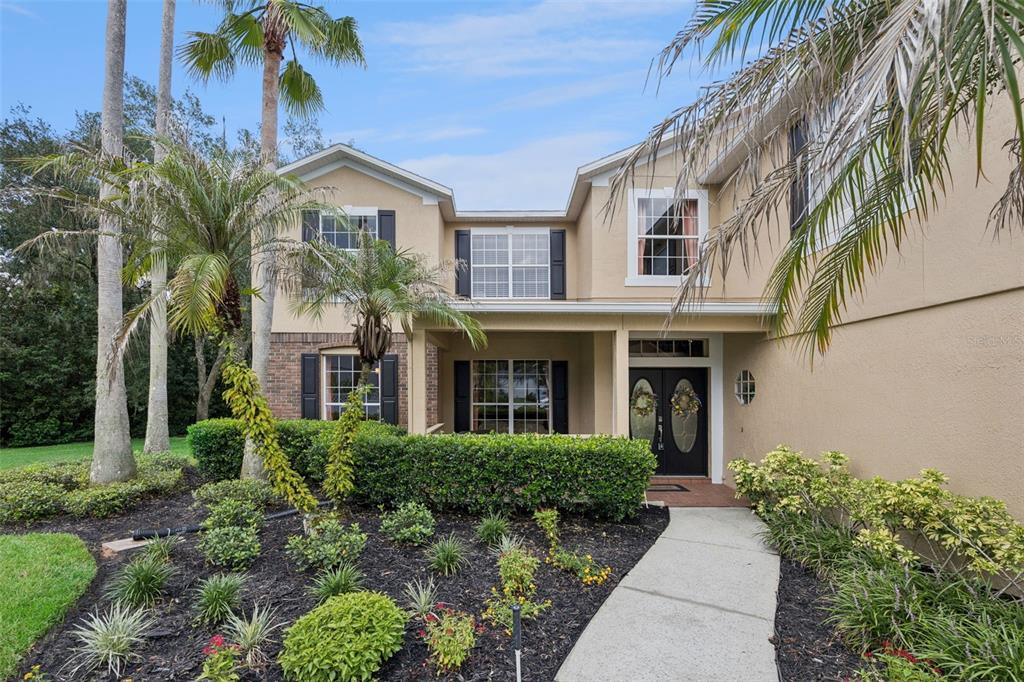 A two-story suburban house with a tan stucco exterior, dark shutters, and a landscaped front yard — 1267 OAKFORD PLACE, OVIEDO, FL