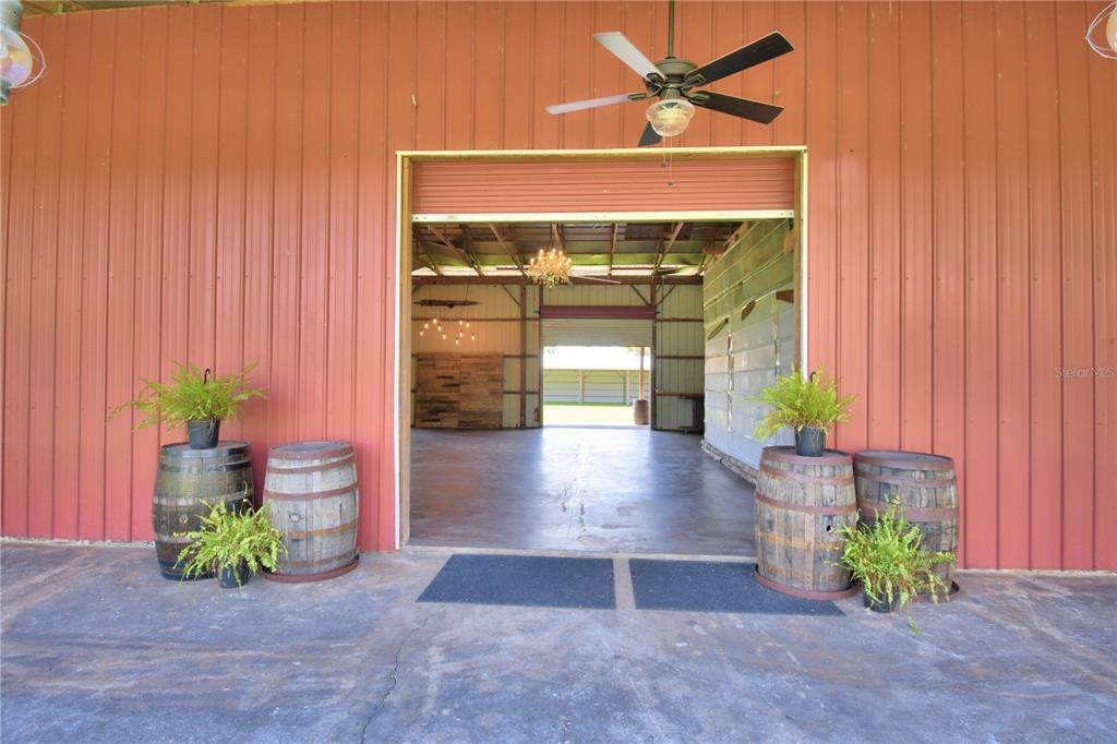 A large open-air barn entrance features red metal siding, wooden barrels, and potted ferns — 5713 LUCERNE PARK ROAD, WINTER HAVEN, FL