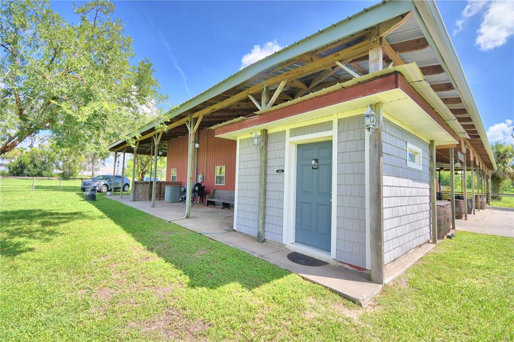 A gray-sided building with a blue door sits under a large, open-air metal roof structure — 5713 LUCERNE PARK ROAD, WINTER HAVEN, FL