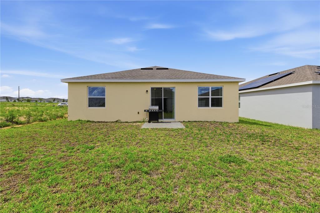 The rear exterior of a single-story house features a tan stucco wall, sliding glass doors, and windows — 740 RICHMOND ESTATE AVENUE, HAINES CITY, FL