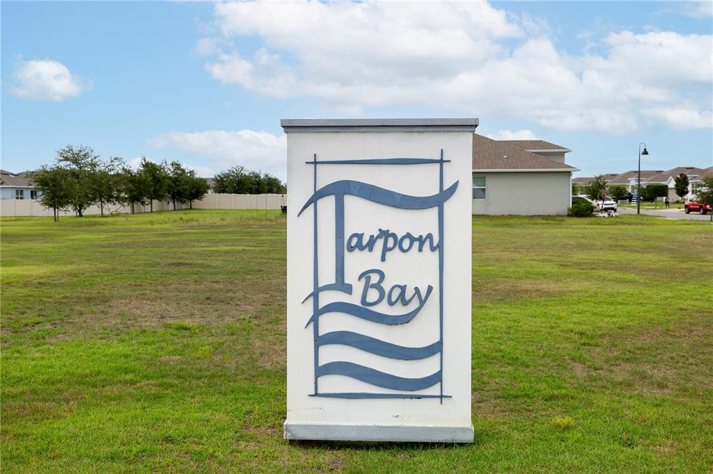 A white monument sign for Tarpon Bay stands in a grassy field near suburban houses — 740 RICHMOND ESTATE AVENUE, HAINES CITY, FL