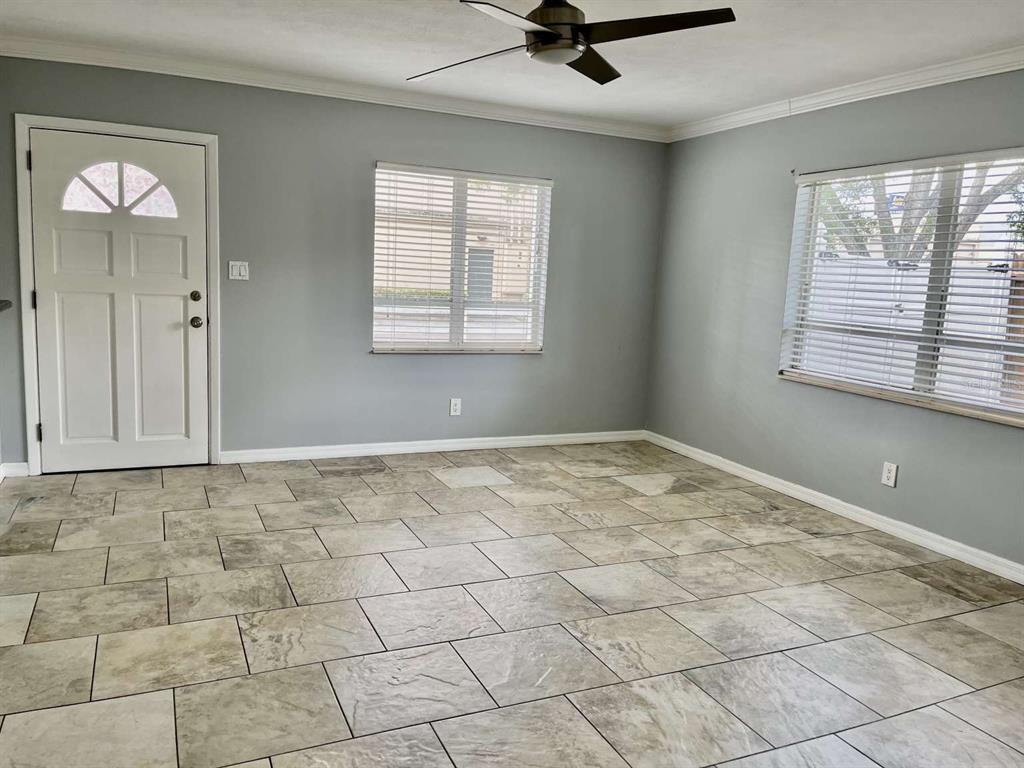 A living room with gray walls, tile flooring, a ceiling fan, and two windows — 116 S RENELLIE DRIVE, TAMPA, FL
