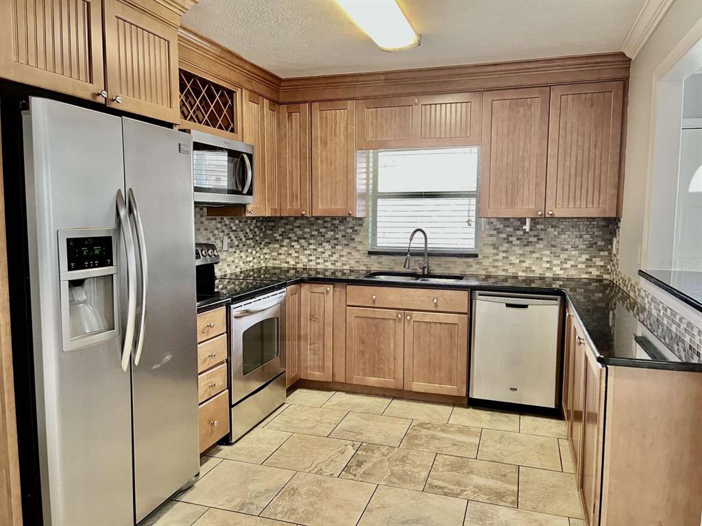 A kitchen features wood cabinets, stainless steel appliances, a tile backsplash, and dark countertops — 116 S RENELLIE DRIVE, TAMPA, FL