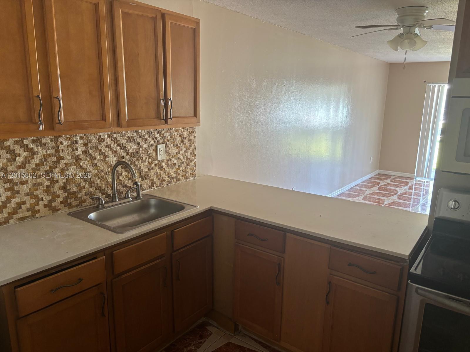 A kitchen features wood cabinets, a stainless steel sink, and a tiled backsplash — 15205 NE 6th Ave # D111, Miami FL 33162, MIAMI, FL