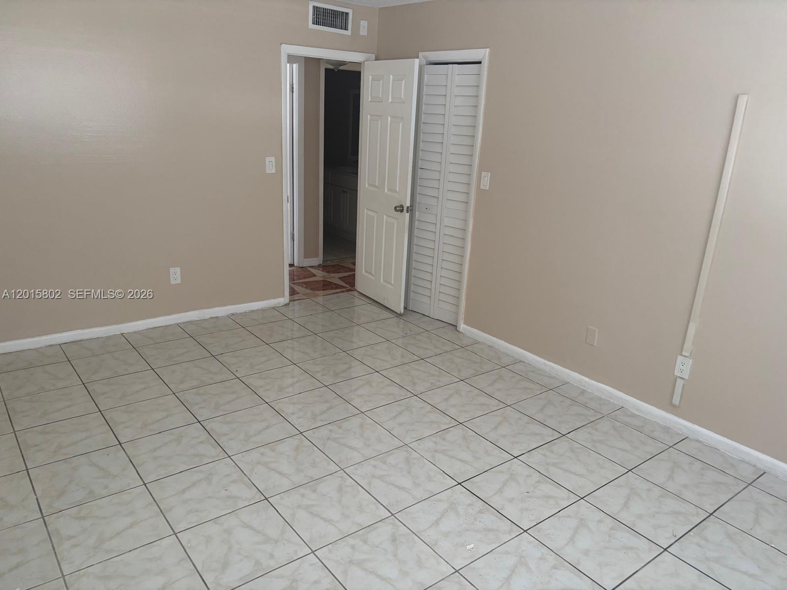 An empty room features beige walls, light-colored tile flooring, and a doorway leading to a bathroom — 15205 NE 6th Ave # D111, Miami FL 33162, MIAMI, FL