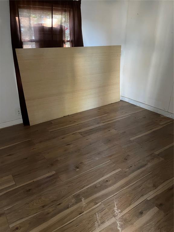 A room with wood-look flooring, white walls, and a large piece of plywood leaning against windows — 16148 BOCA RATON STREET, BROOKSVILLE, FL