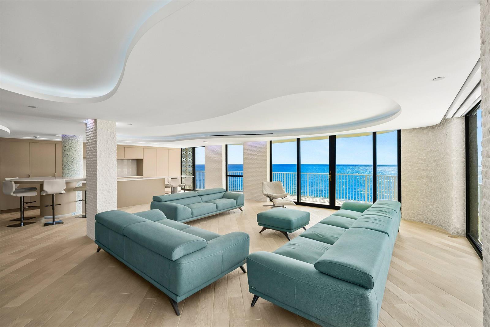 A modern living room features teal sofas, light wood floors, and floor-to-ceiling ocean views — 3360 S Ocean Boulevard # i, Palm Beach FL 33480, PALM BEACH, FL