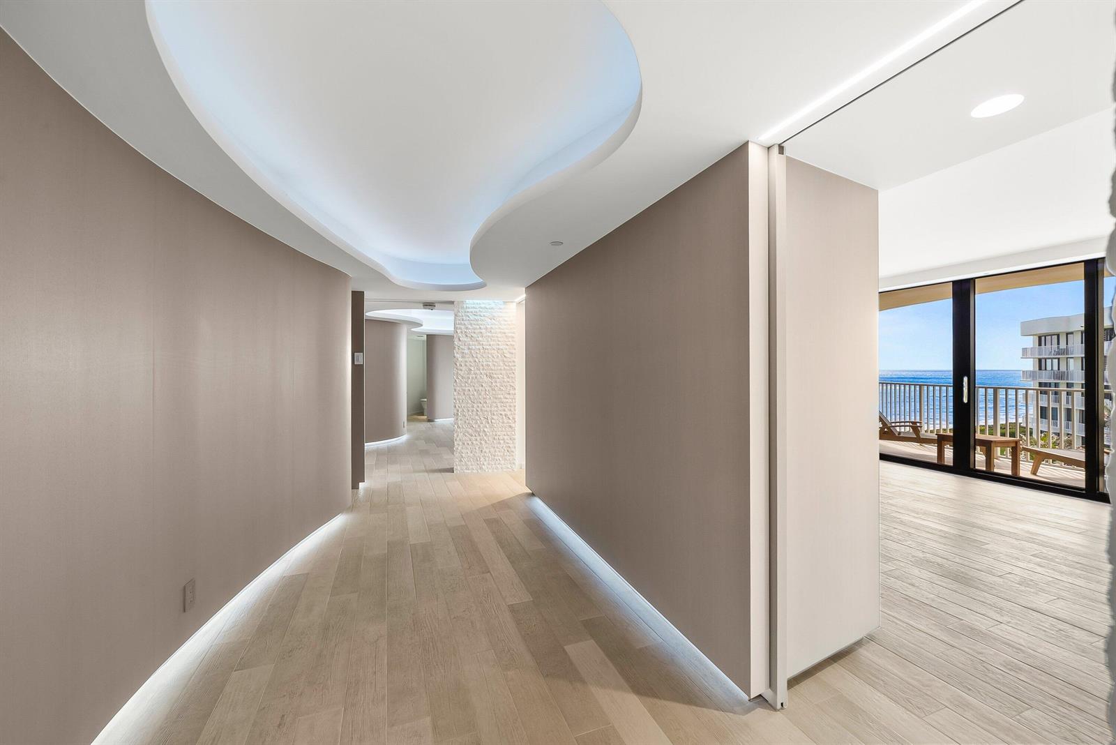 A modern hallway with curved ceiling lighting, wood-look flooring, and a view of the ocean — 3360 S Ocean Boulevard # i, Palm Beach FL 33480, PALM BEACH, FL