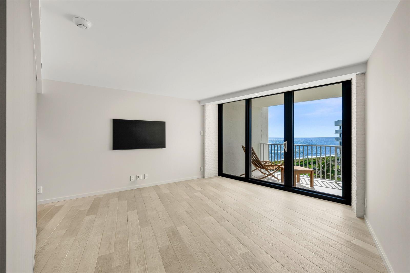 An empty room with light wood floors, a wall-mounted television, and a balcony overlooking ocean — 3360 S Ocean Boulevard # i, Palm Beach FL 33480, PALM BEACH, FL