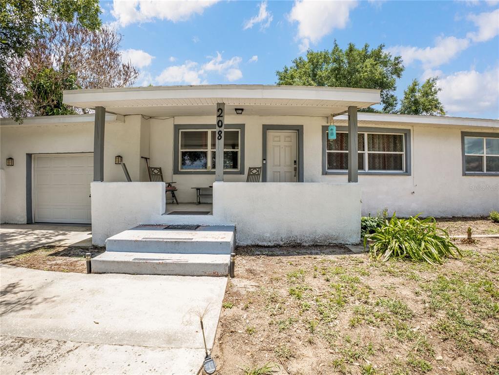 A single-story house with a white stucco exterior, a covered front porch, and a garage — 208 E WINTHROP STREET, AVON PARK, FL