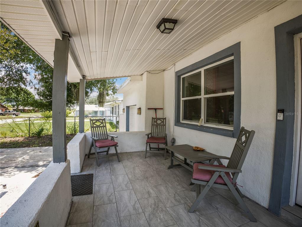 A covered porch features tiled flooring, three wooden chairs, a small table, and white walls — 208 E WINTHROP STREET, AVON PARK, FL