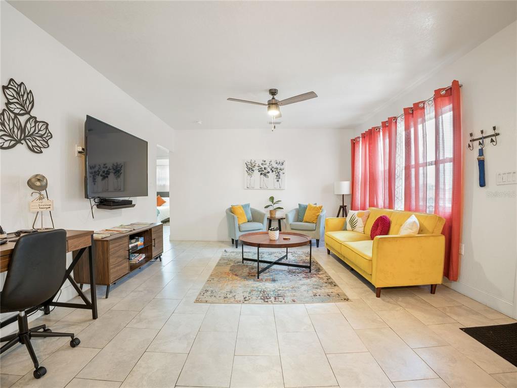A living room with tile floors, a yellow sofa, two armchairs, and a wall-mounted television — 208 E WINTHROP STREET, AVON PARK, FL