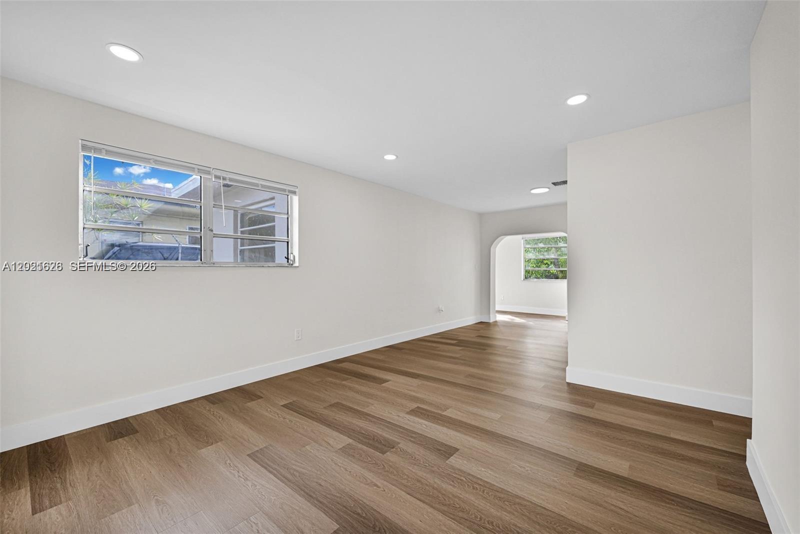 An empty room features light-colored walls, recessed lighting, and wood-look flooring with an arched doorway — 11810 NE 14th Ave # 11810, Miami FL 33161, MIAMI, FL