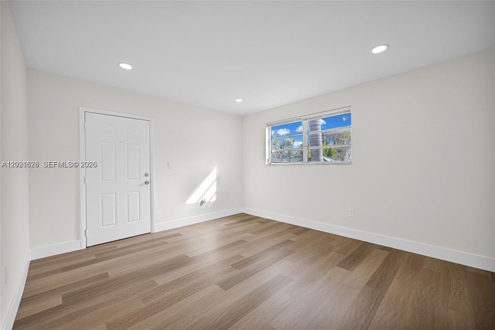 An empty room features light-colored walls, wood-look flooring, a white door, and a window — 11810 NE 14th Ave # 11810, Miami FL 33161, MIAMI, FL