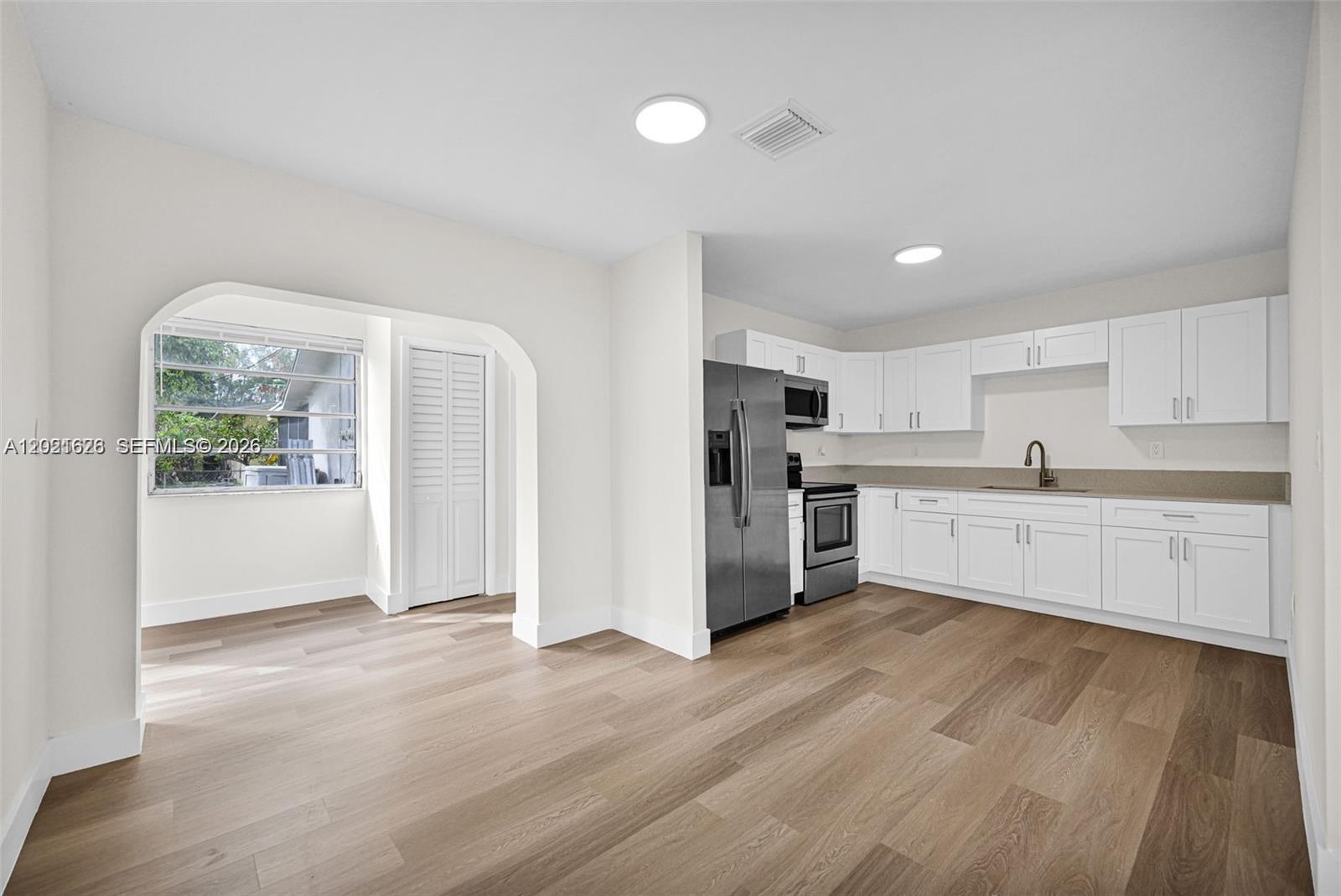 A kitchen with white cabinets and stainless steel appliances opens into a dining area — 11810 NE 14th Ave # 11810, Miami FL 33161, MIAMI, FL