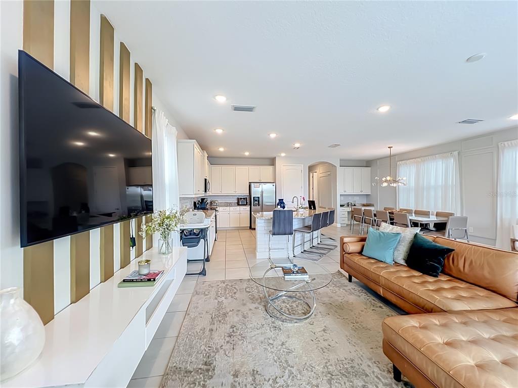 An open-concept living room and kitchen featuring a leather sectional, television, and white cabinetry — 272 SOUTHFIELD STREET, KISSIMMEE, FL