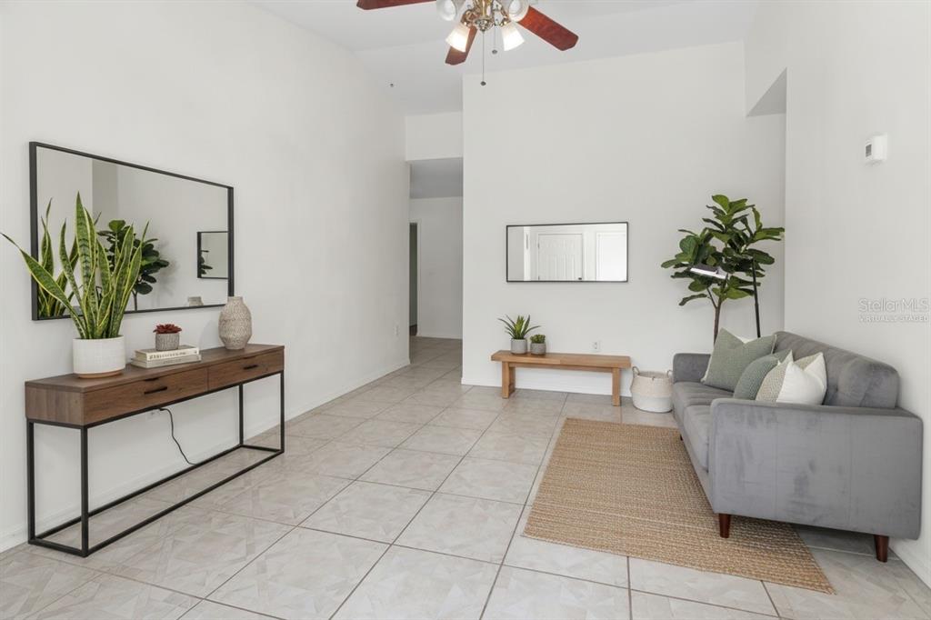 A living room with tile floors, a gray sofa, a console table, and wall mirrors — 4715 4TH AVENUE E, PALMETTO, FL