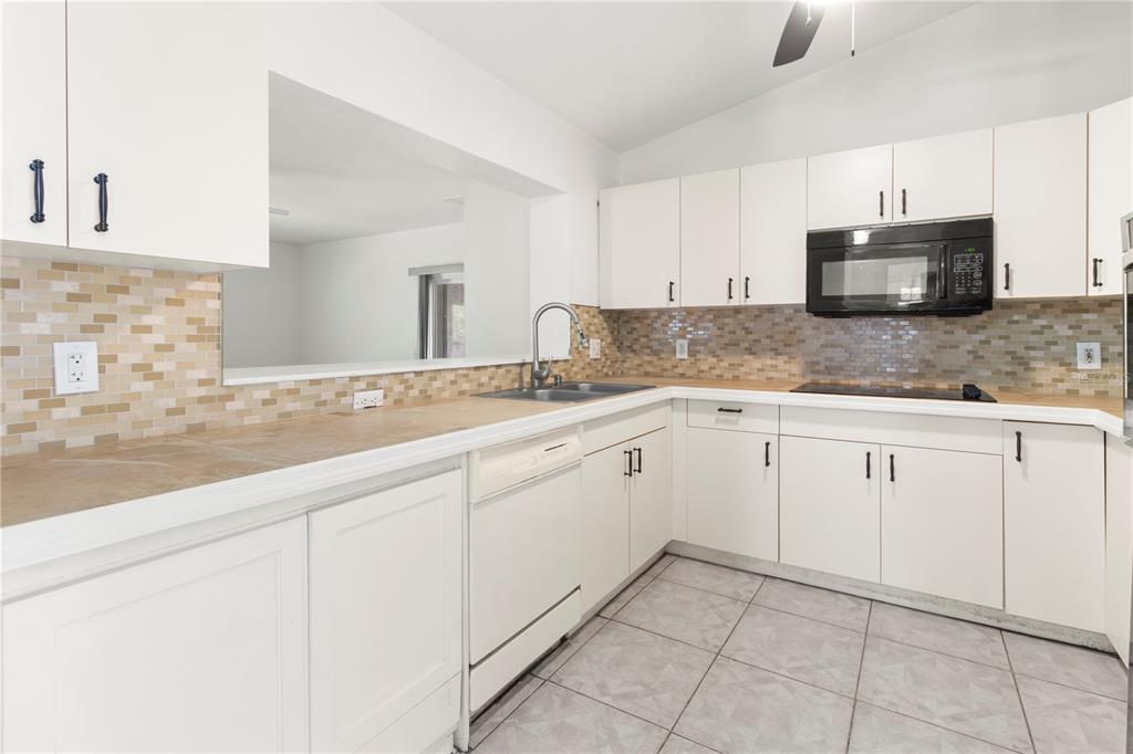 A kitchen with white cabinets, a tiled backsplash, a dishwasher, and a microwave — 4715 4TH AVENUE E, PALMETTO, FL