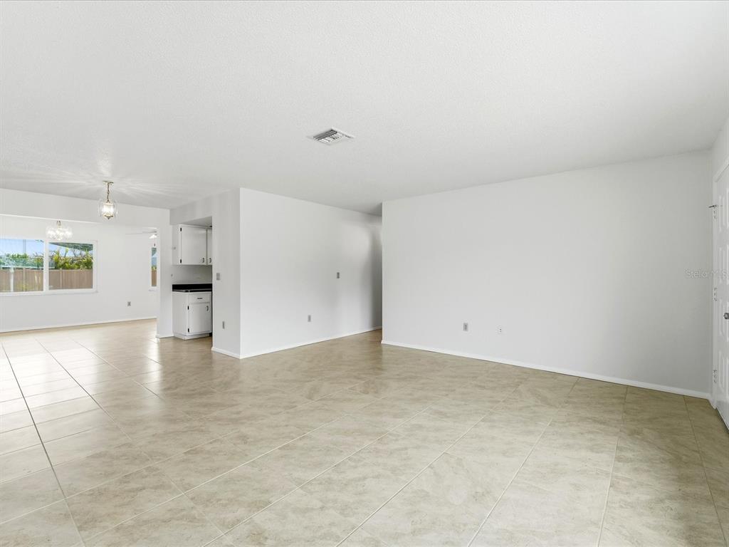 An open-concept living area with white walls and light-colored tile flooring leads to a kitchen — 21029 PEACHLAND BOULEVARD, PORT CHARLOTTE, FL
