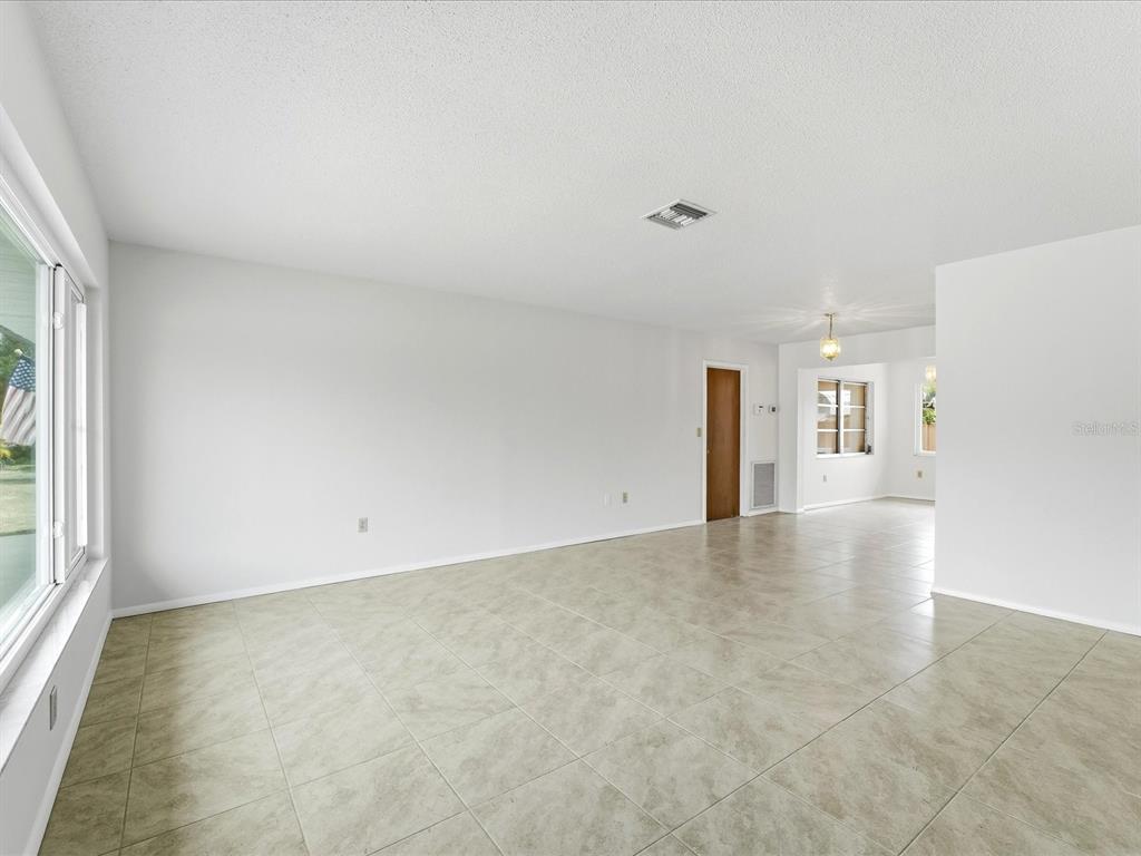 A bright, empty living room features white walls, light tile flooring, and a large window — 21029 PEACHLAND BOULEVARD, PORT CHARLOTTE, FL