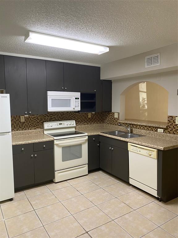 A kitchen features dark cabinets, beige countertops, a tiled backsplash, and white appliances — 130 RHODEN LANE, WINTER SPRINGS, FL