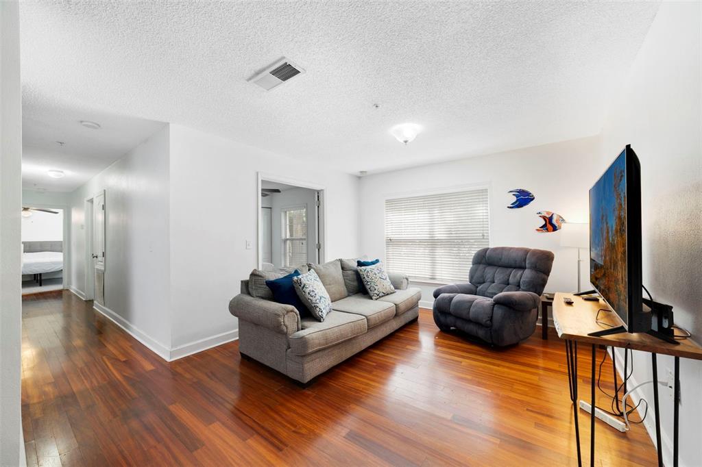 A living room features hardwood floors, a gray sofa, a recliner, and a television stand — 2019 DIXIE BELLE DRIVE UNIT G, ORLANDO, FL