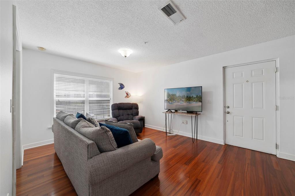 A living room features hardwood floors, a gray sofa, a recliner, and a wall-mounted television — 2019 DIXIE BELLE DRIVE UNIT G, ORLANDO, FL