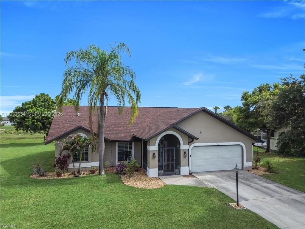A single-story house with a brown shingled roof, beige stucco exterior, and a palm tree — 538 Whispering Wind Bnd, Lehigh Acres FL 33974, LEHIGH ACRES, FL