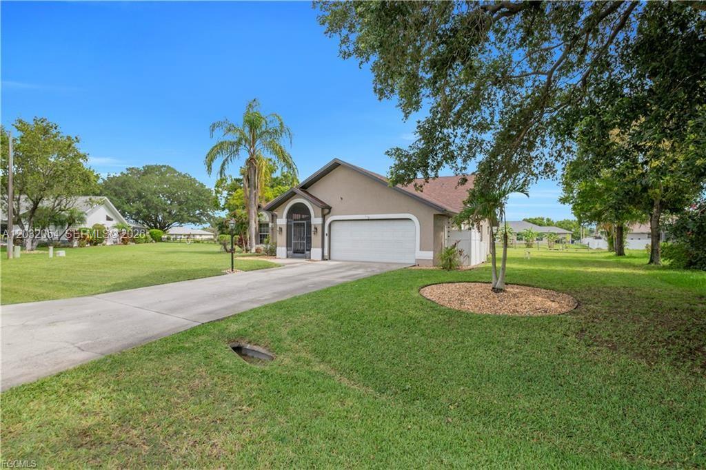 A single-story house with a white garage door and a concrete driveway sits on grass — 538 Whispering Wind Bnd, Lehigh Acres FL 33974, LEHIGH ACRES, FL