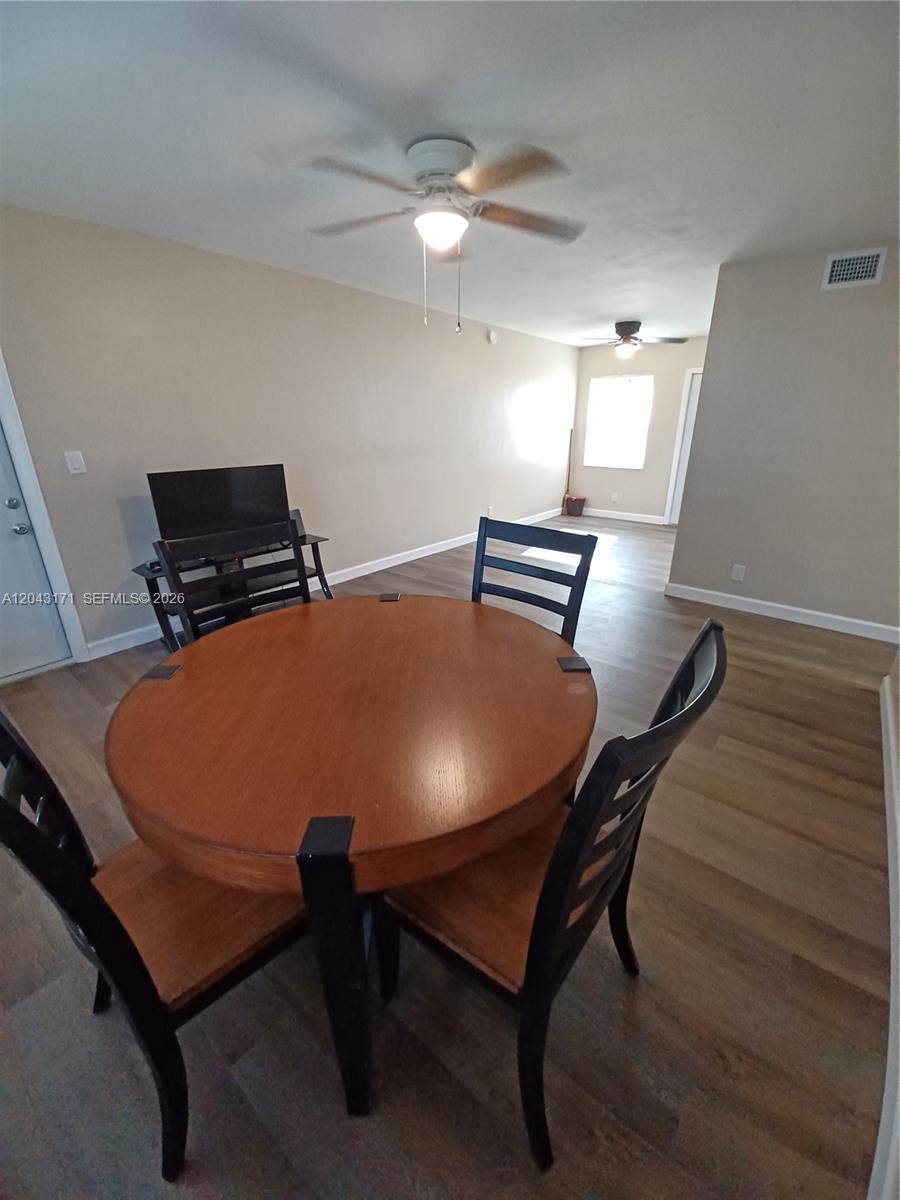 A dining area features a round wooden table, black chairs, and light-colored wood-look flooring — HOLLYWOOD, FL