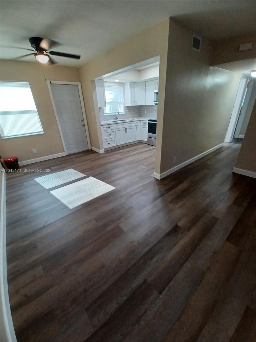 An open-concept living area features dark wood-look flooring and a view into a white kitchen — HOLLYWOOD, FL