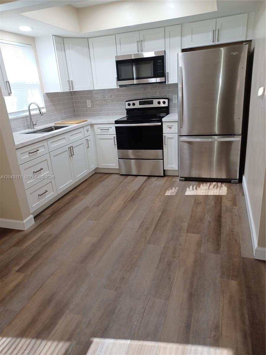 A kitchen features white cabinets, stainless steel appliances, gray subway tile, and wood-look flooring — HOLLYWOOD, FL