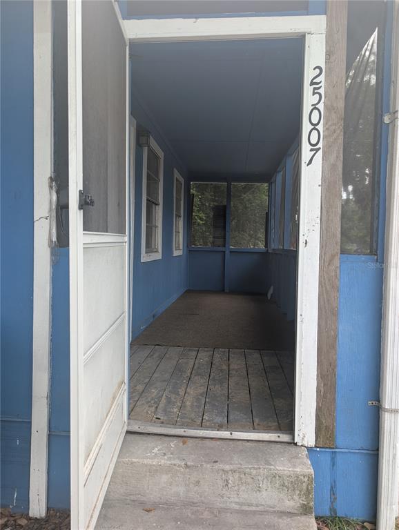 A view through an open screen door into a blue-painted, covered porch with wooden flooring — 25007 NW 6TH AVENUE, NEWBERRY, FL