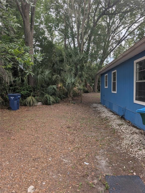 A side view of a blue house exterior with a yard, trees, and a trash bin — 25007 NW 6TH AVENUE, NEWBERRY, FL