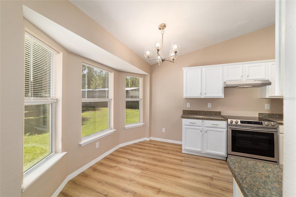 A kitchen with white cabinets, stainless steel appliances, wood-look flooring, and a dining nook — 5315 SE 26TH AVENUE, OCALA, FL