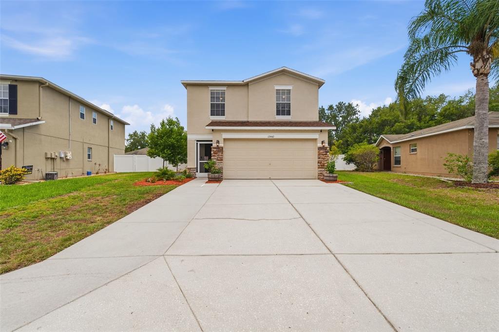 A two-story suburban house with a concrete driveway, a two-car garage, and a palm tree — 12442 SAULSTON PLACE, HUDSON, FL