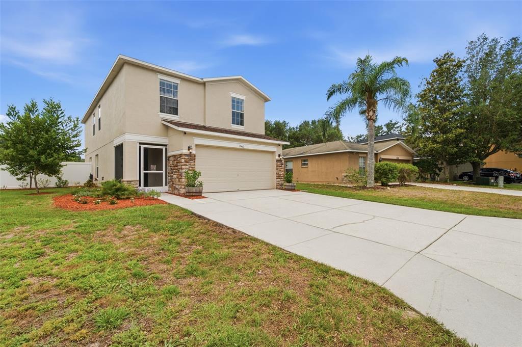 A two-story suburban house with a beige stucco exterior, stone accents, and a concrete driveway — 12442 SAULSTON PLACE, HUDSON, FL