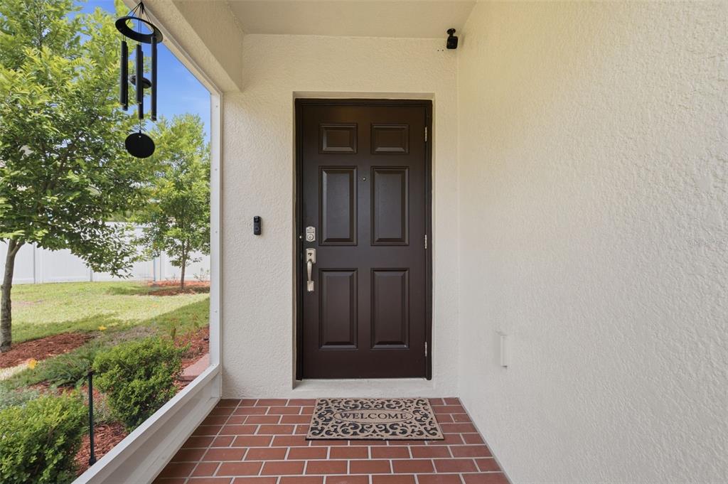 A brown front door with a welcome mat sits on a brick porch — 12442 SAULSTON PLACE, HUDSON, FL