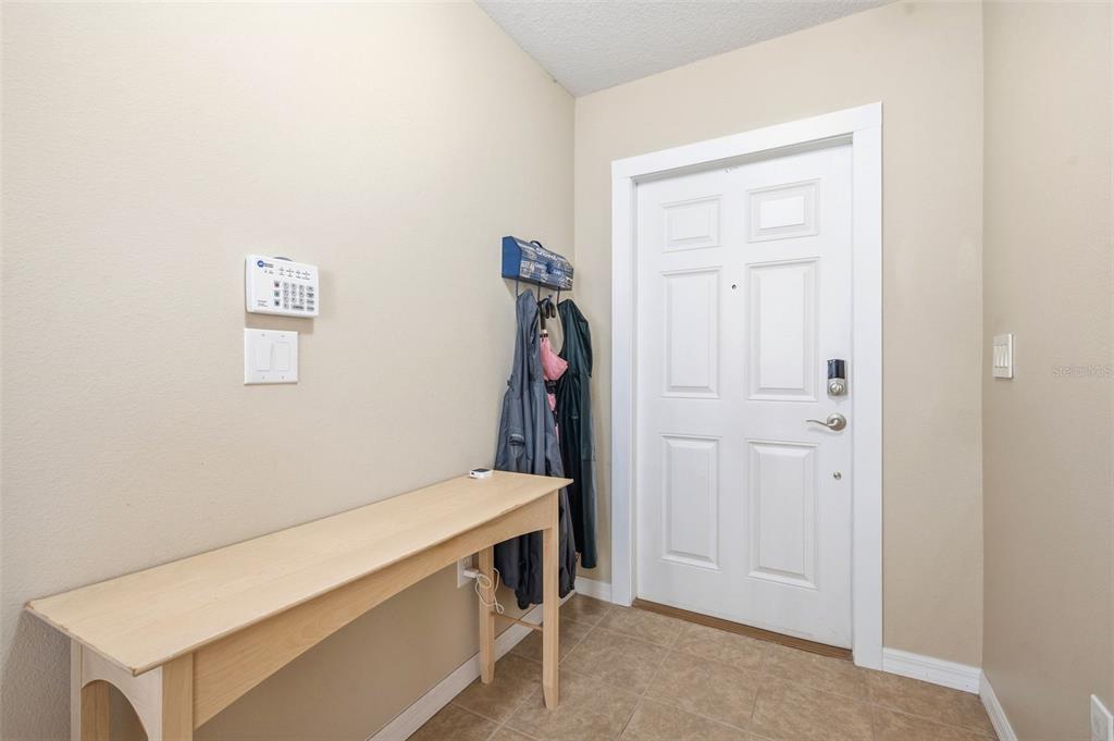 An entryway features a light wood console table, a wall-mounted security panel, and a white door — 12442 SAULSTON PLACE, HUDSON, FL