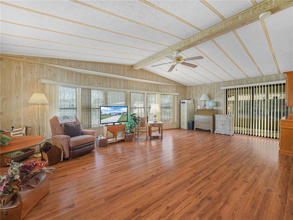 A living room with wood-paneled walls, wood-look flooring, a ceiling fan, and large windows — 1679 FOXWAY DRIVE, LAKELAND, FL