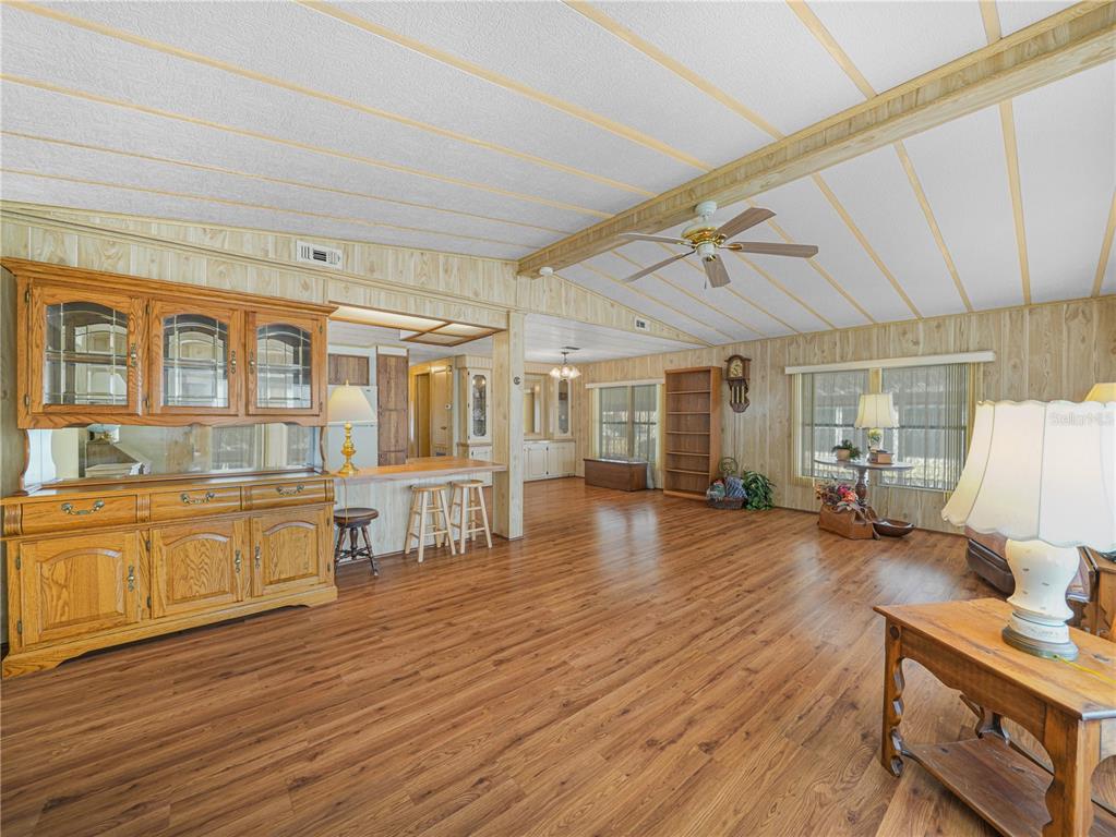A spacious living room with wood-paneled walls, wood-look flooring, a ceiling fan, and built-in cabinetry — 1679 FOXWAY DRIVE, LAKELAND, FL