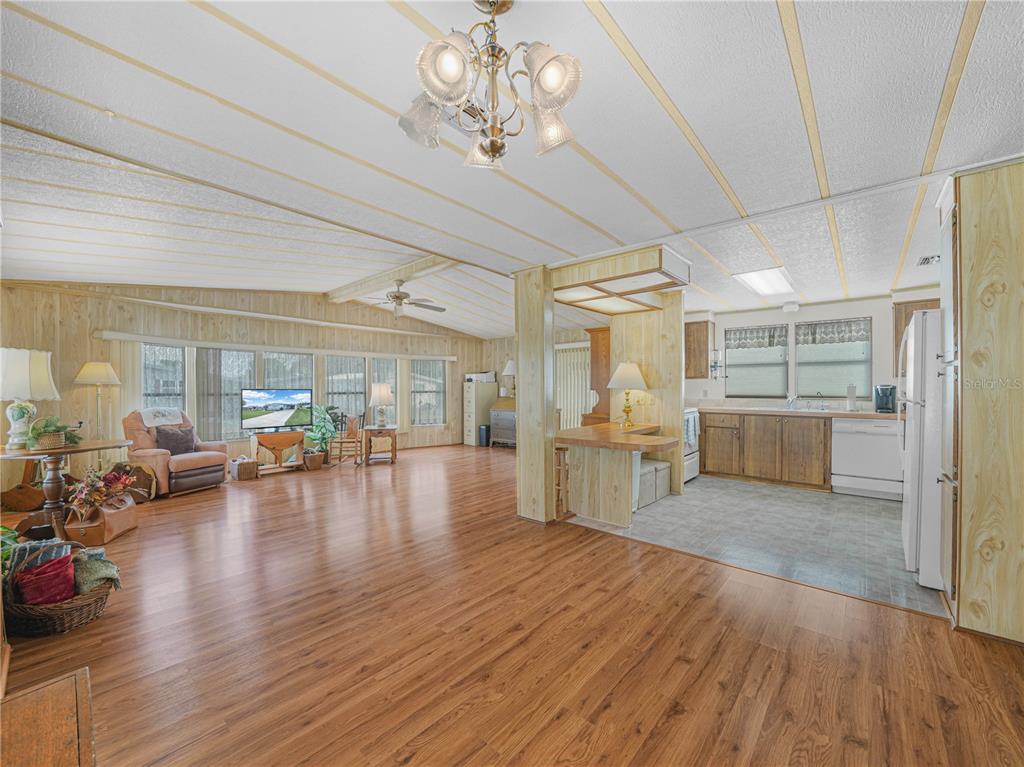 An open-concept living room and kitchen featuring wood-paneled walls and laminate flooring — 1679 FOXWAY DRIVE, LAKELAND, FL