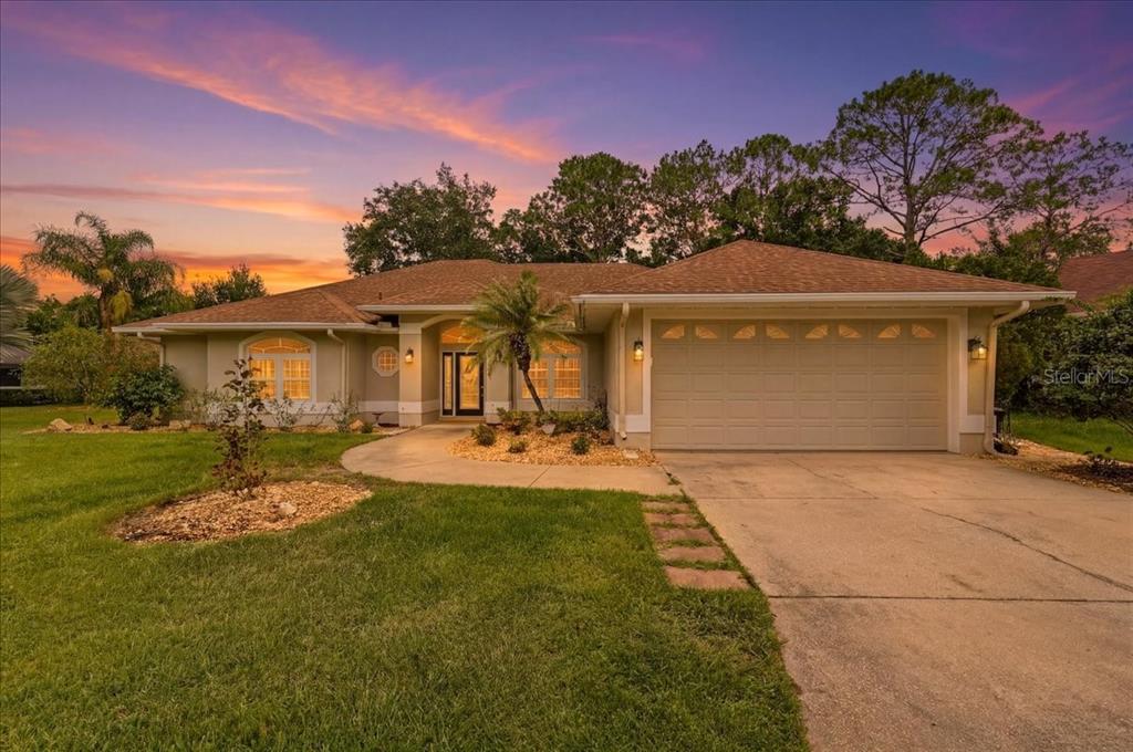 A single-story suburban house with a two-car garage and a paved walkway at sunset — 3158 BEAUCHAMP COURT, WINTER HAVEN, FL