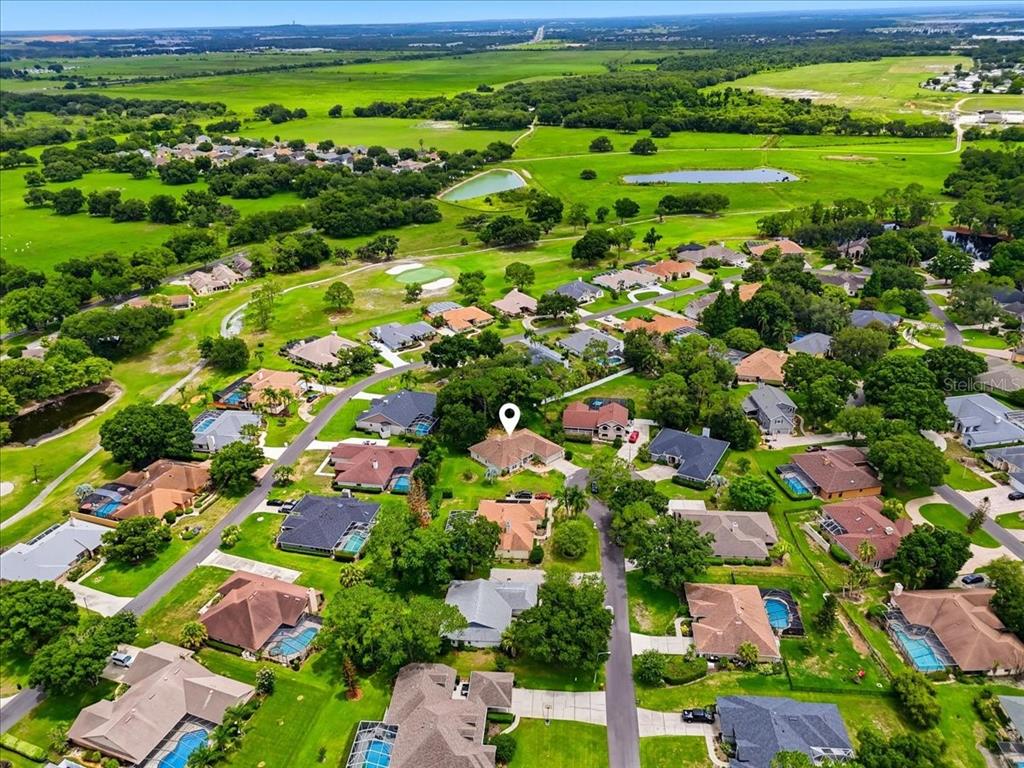 An aerial view shows a suburban neighborhood with houses, swimming pools, and surrounding green fields — 3158 BEAUCHAMP COURT, WINTER HAVEN, FL