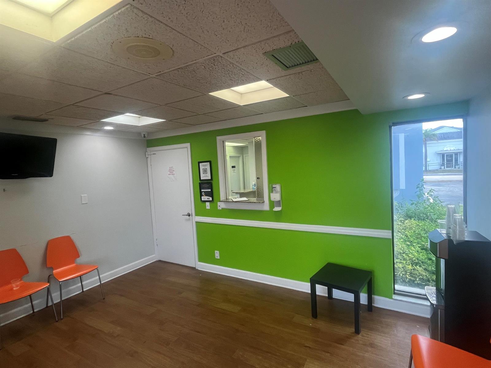 A waiting room features orange chairs, a green accent wall, wood flooring, and a window — 1708 N Federal Highway, FL 33460, FL