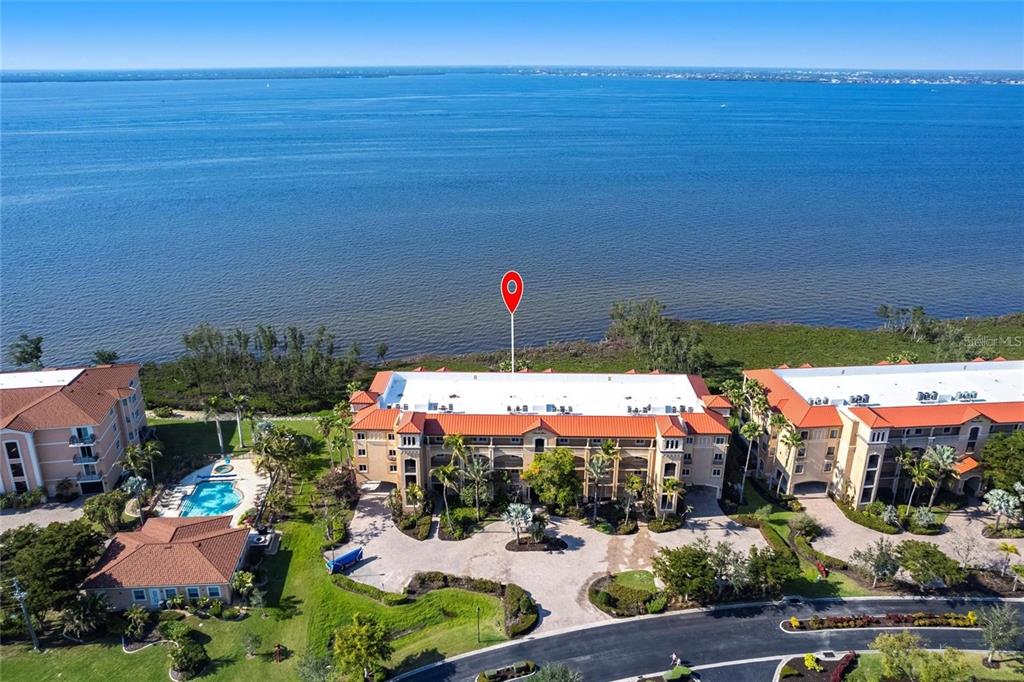 An aerial view shows a multi-story apartment building with a red tile roof near water — 93 VIVANTE BLVD UNIT 9323, PUNTA GORDA, FL