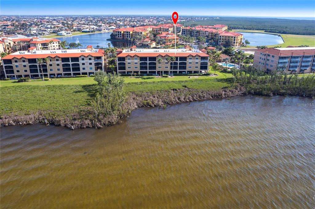 An aerial view shows a multi-story apartment building situated along a waterfront with vegetation — 93 VIVANTE BLVD UNIT 9323, PUNTA GORDA, FL