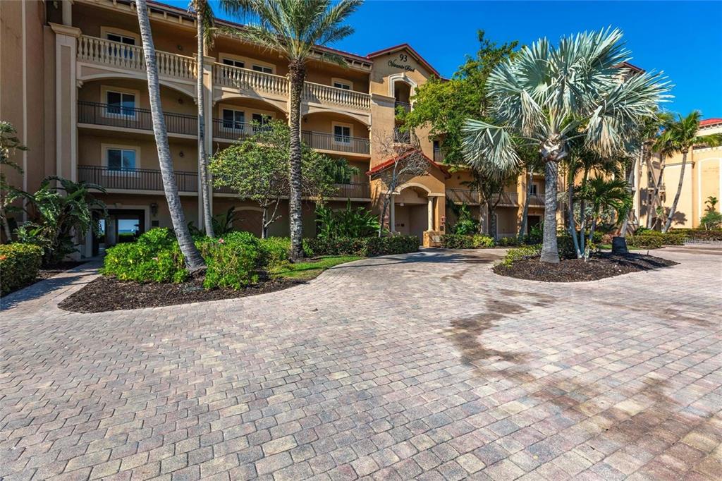 A multi-story tan stucco apartment building with balconies and palm trees over a paved driveway — 93 VIVANTE BLVD UNIT 9323, PUNTA GORDA, FL